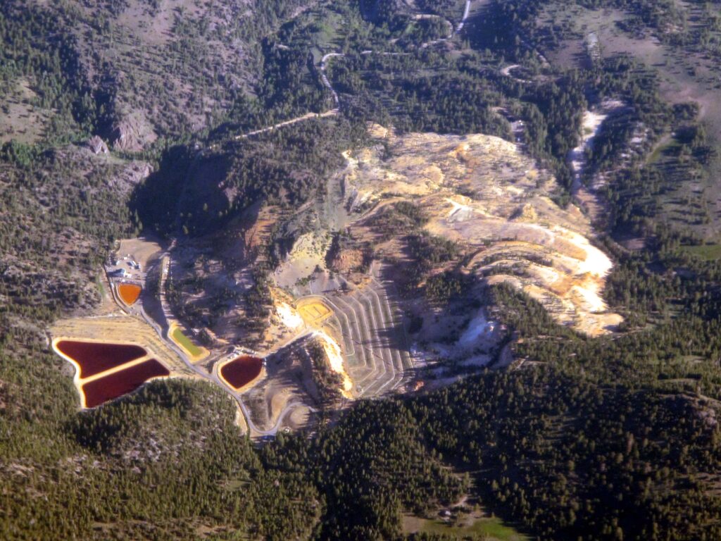 Aerial view of the open-pit Leviathan Mine and its coloured treatment ponds in forested hills